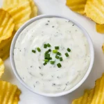 Low FODMAP ranch dressing in white bowl with fresh chives, surrounded by golden potato chips