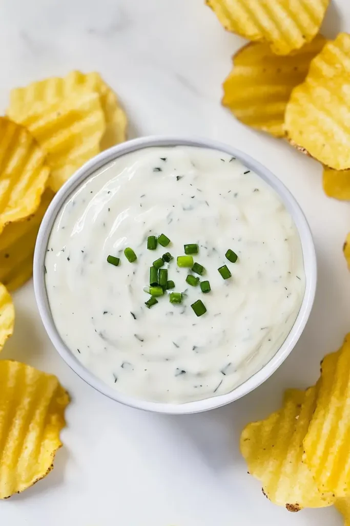 Low FODMAP ranch dressing in white bowl with fresh chives, surrounded by golden potato chips