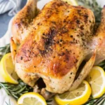 Golden Low FODMAP Roasted Lemon Chicken with crispy skin on white platter with fresh lemon and rosemary