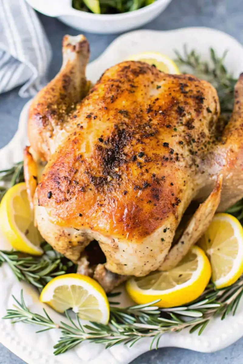 Golden Low FODMAP Roasted Lemon Chicken with crispy skin on white platter with fresh lemon and rosemary